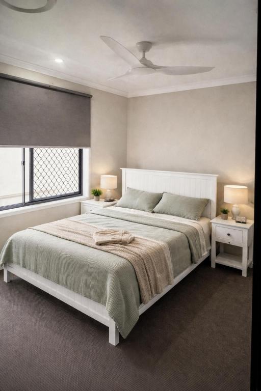a white bedroom with a large bed and a window at Comfortable Home stay in Pimpama