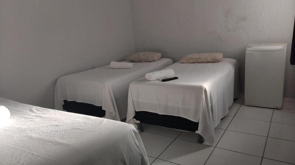 een kamer met 2 bedden met witte lakens en een koelkast bij Pousada praia avenida in Maceió