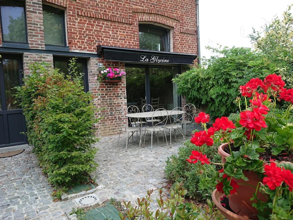 ein Backsteingebäude mit einer Terrasse mit roten Blumen in der Unterkunft Gîtes de la maison du haras in Beuvron-en-Auge