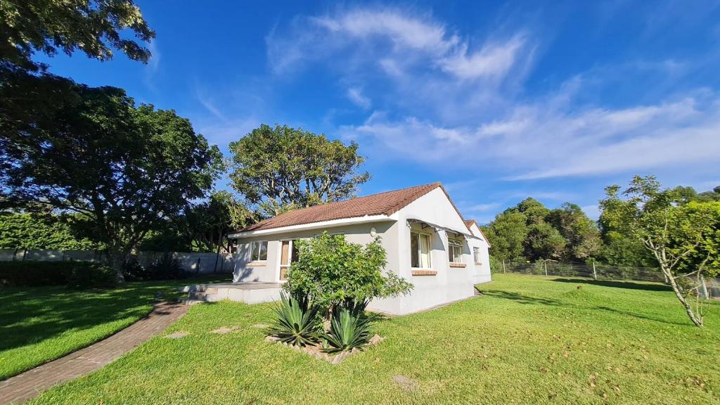 a small white house in a grassy yard at Flanders South Cottage in Gqeberha