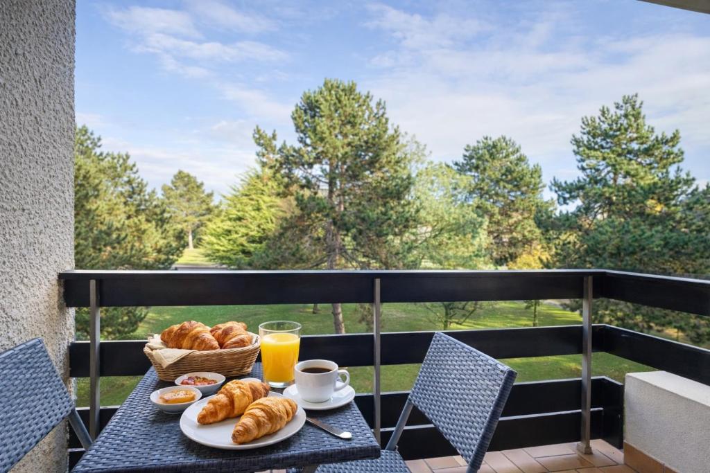 a table with a breakfast of croissants and orange juice at Appartement deux pièces élégant avec Vue sur Parc - Plage & Centre-Ville à Pied in Cabourg