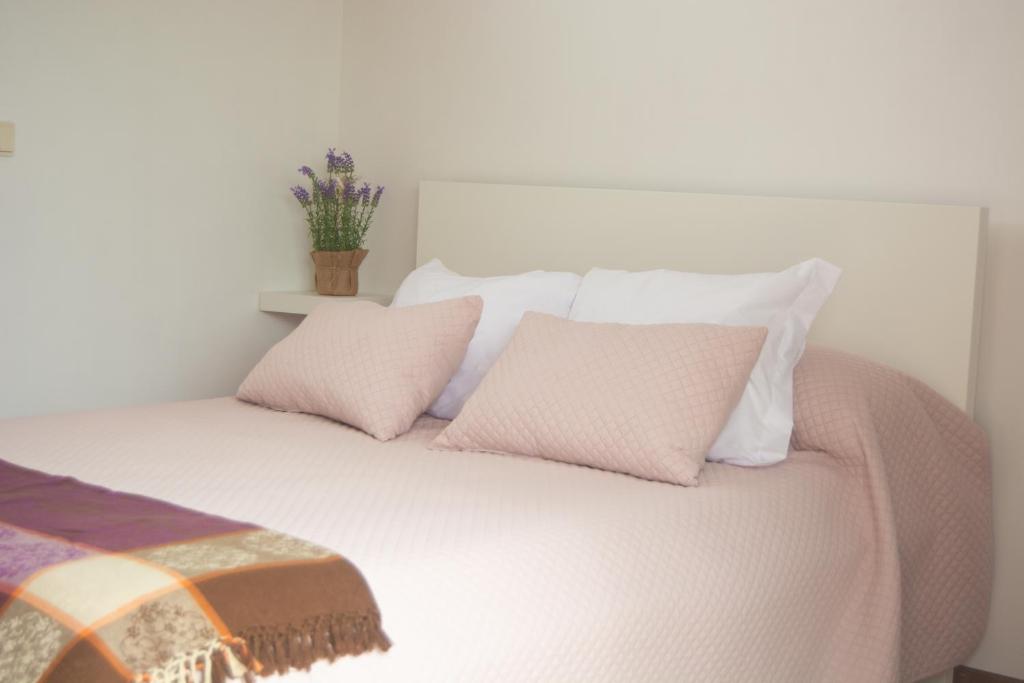 un letto con cuscini rosa e bianchi e una pianta in vaso di Cantinho da Celeste a Paramos