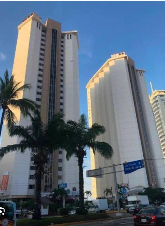 two tall buildings with palm trees in a city at Torres Gemelas Costera MA con Playa Privada in Acapulco
