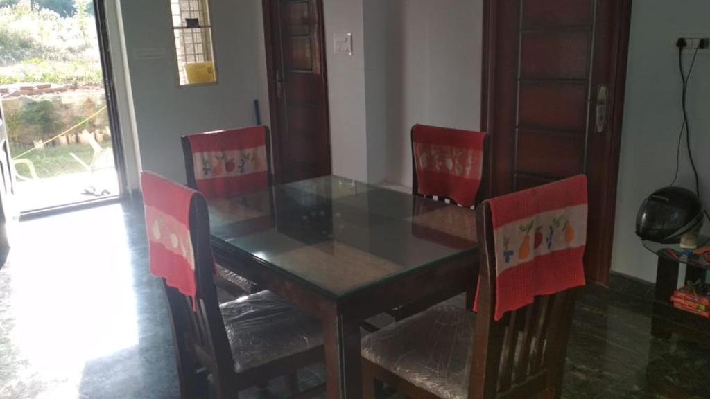 een eettafel met 2 stoelen, een glazen tafel en een stoeltje bij Peacock Abode Farm in Bangalore