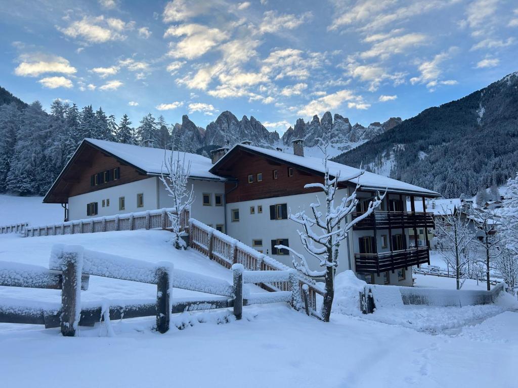 ein schneebedecktes Gebäude mit einem Zaun in der Unterkunft MiraOdle Apartments in Villnöß