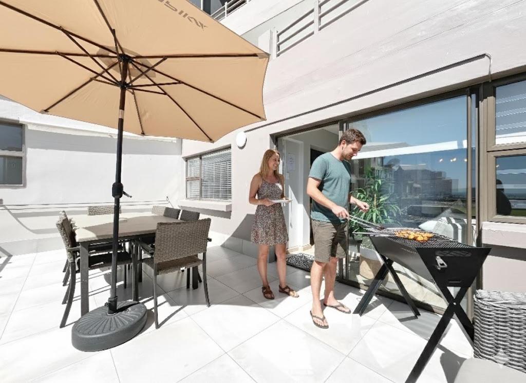 Un homme et une femme debout sur une terrasse avec un parasol dans l'établissement Coastal Hospitality - De Valle 24, à Mossel Bay