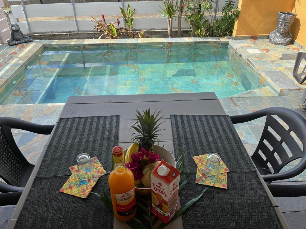 a table with drinks on it next to a swimming pool at VILLA COLIBRI Piscine balnéo privative in Sainte-Rose
