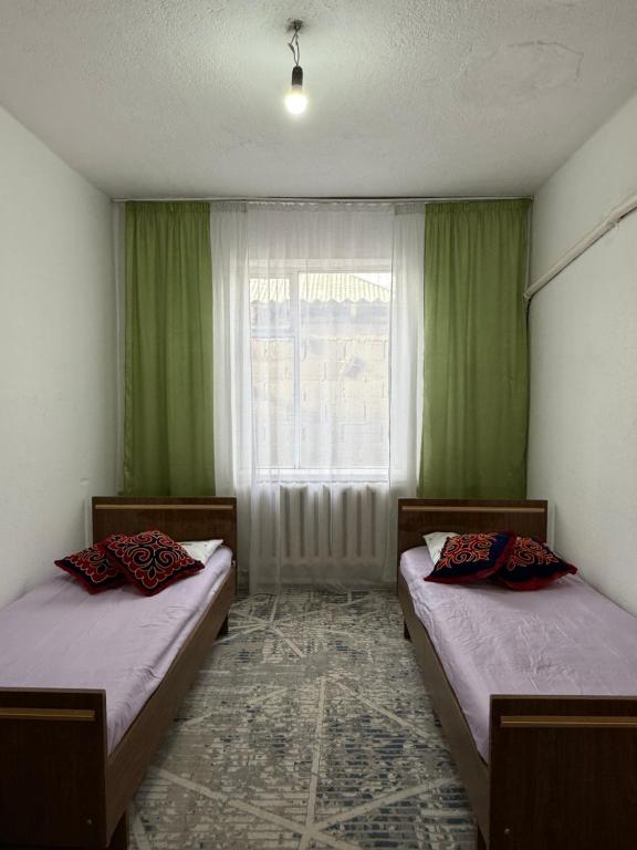 twee bedden in een kamer met groene gordijnen en een raam bij Ali Guest House in Kara-Koo