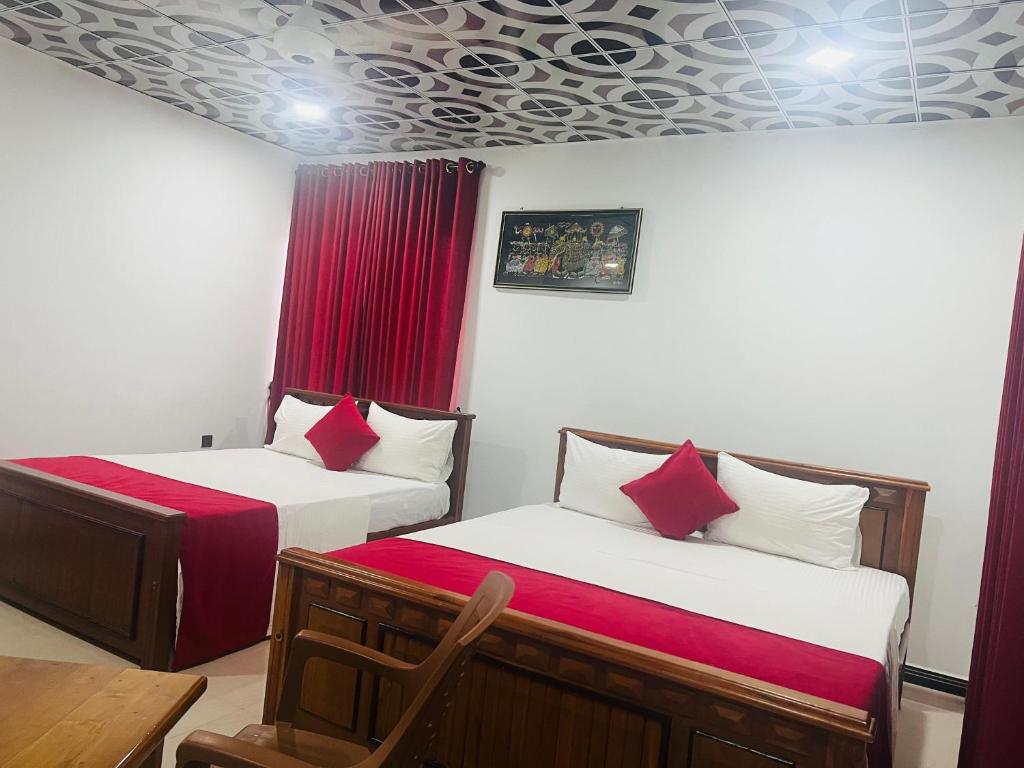 two beds in a room with red curtains at Uthaya Guest House in Mullaittivu