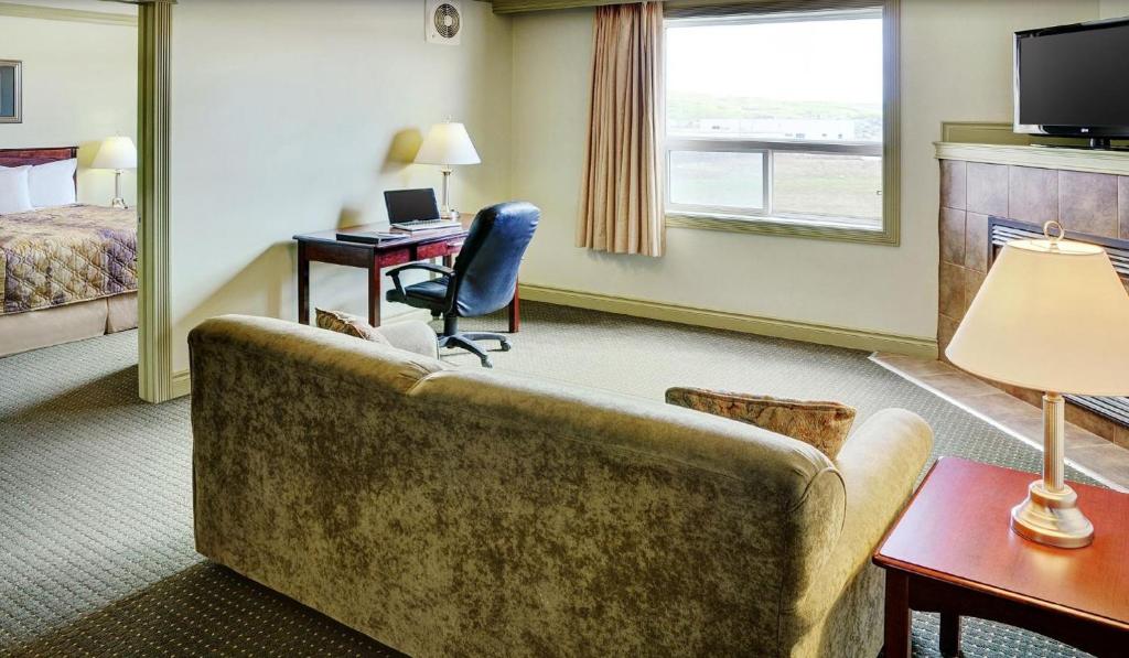 a hotel room with a couch and a desk and a bed at Nova Inn Peace River in Peace River