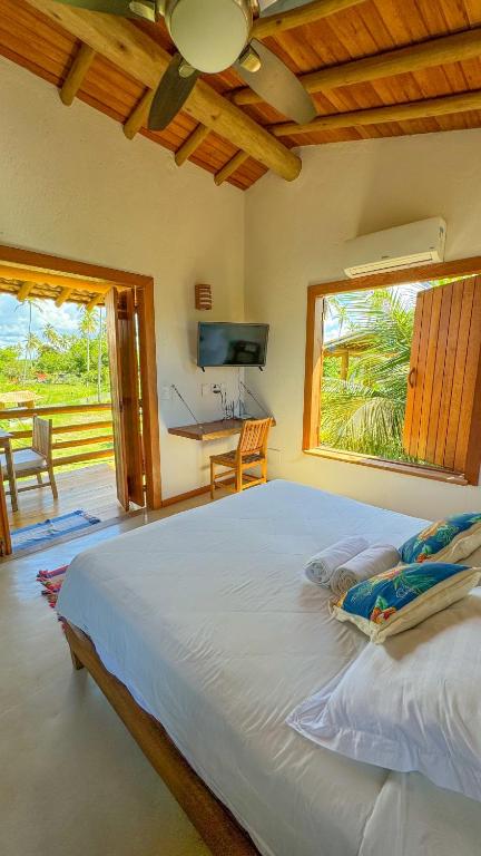 a bedroom with a large bed with a desk and a window at Vila Budião - Corumbau in Corumbau