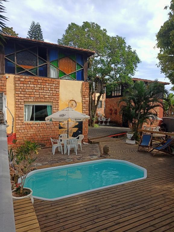 a pool with a table and an umbrella and a house at Pousada Gendra's in Imbituba