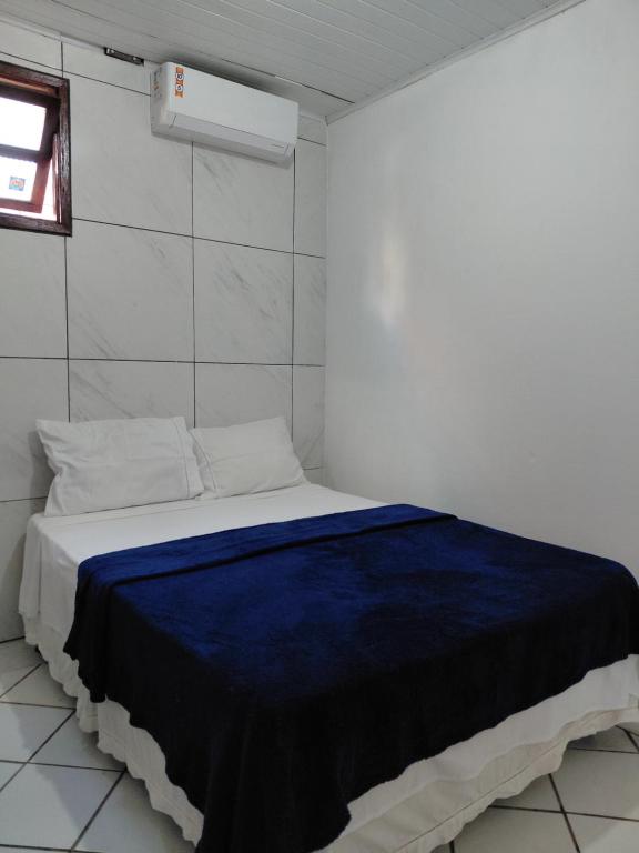 een witte kamer met een bed met een blauwe deken bij Hostel Aki in Itacaré