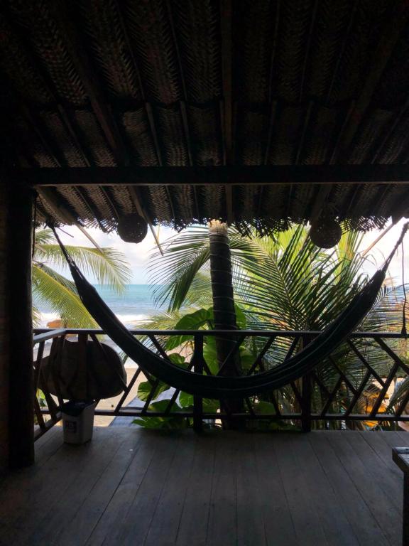a hammock on a deck with a palm tree at Puerto Manglar Hostal in Guachaca