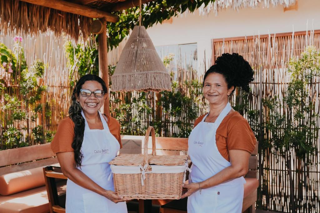 Twee vrouwen staan naast elkaar en houden een mand vast. bij Pousada Casa Buriti - Atins in Atins