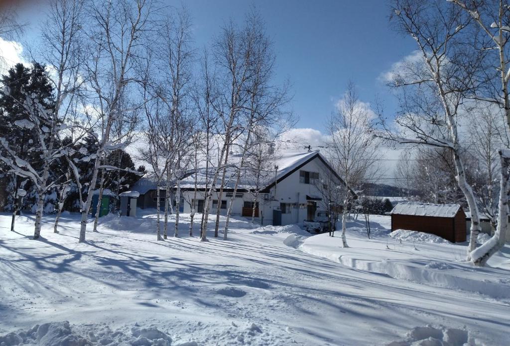 a snow covered yard with a house and trees at プチキャンプ場おちぼの郷 in Furano