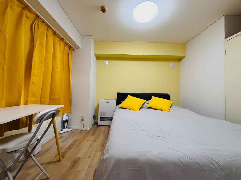 ein Schlafzimmer mit einem Bett mit gelben Kissen und einem Schreibtisch in der Unterkunft 501札幌駅と大通駅も徒歩圏内な最高な立地最大2名様まで快適にご宿泊可能です in Sapporo