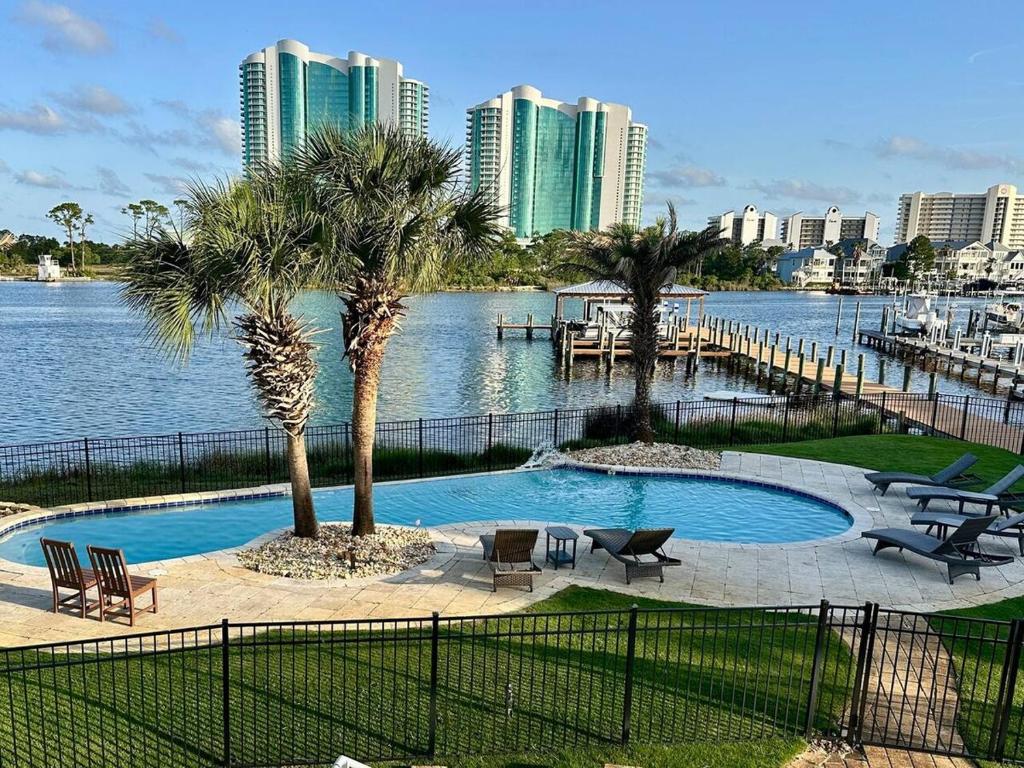 a pool with palm trees and chairs next to a body of water at Bayou Breeze Retreat in Orange Beach