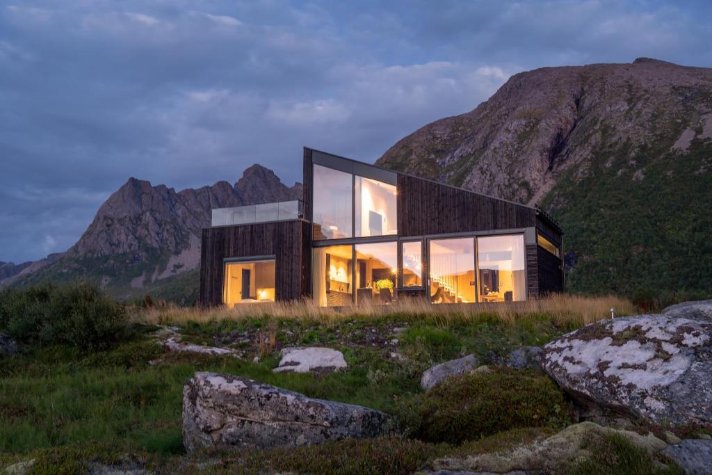 a house on a hill with mountains in the background at Hoda Cabin - Luxury lodge with jacuzzi and sauna in Lyngværet
