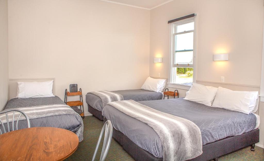 een kamer met twee bedden, een tafel en een raam bij Hokitika Pioneer Hotel in Hokitika