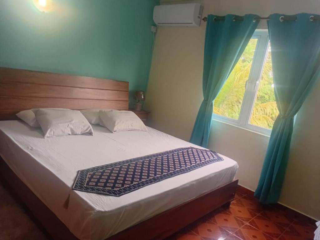 een slaapkamer met een bed en een raam met blauwe gordijnen bij Shantee Residence in Trou dʼ Eau Douce