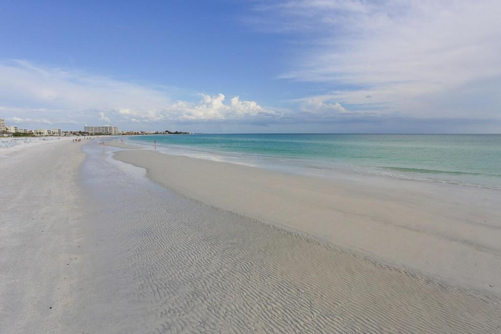 an empty beach with people walking on the water at 2BR Renovated Siesta Key Condo, beach and pool access in Sarasota