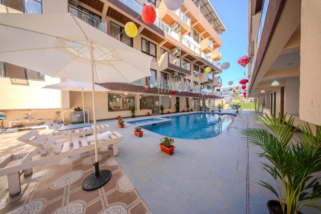 a hotel with a swimming pool and an umbrella at La Bela Casa Suites, Candolim in Candolim