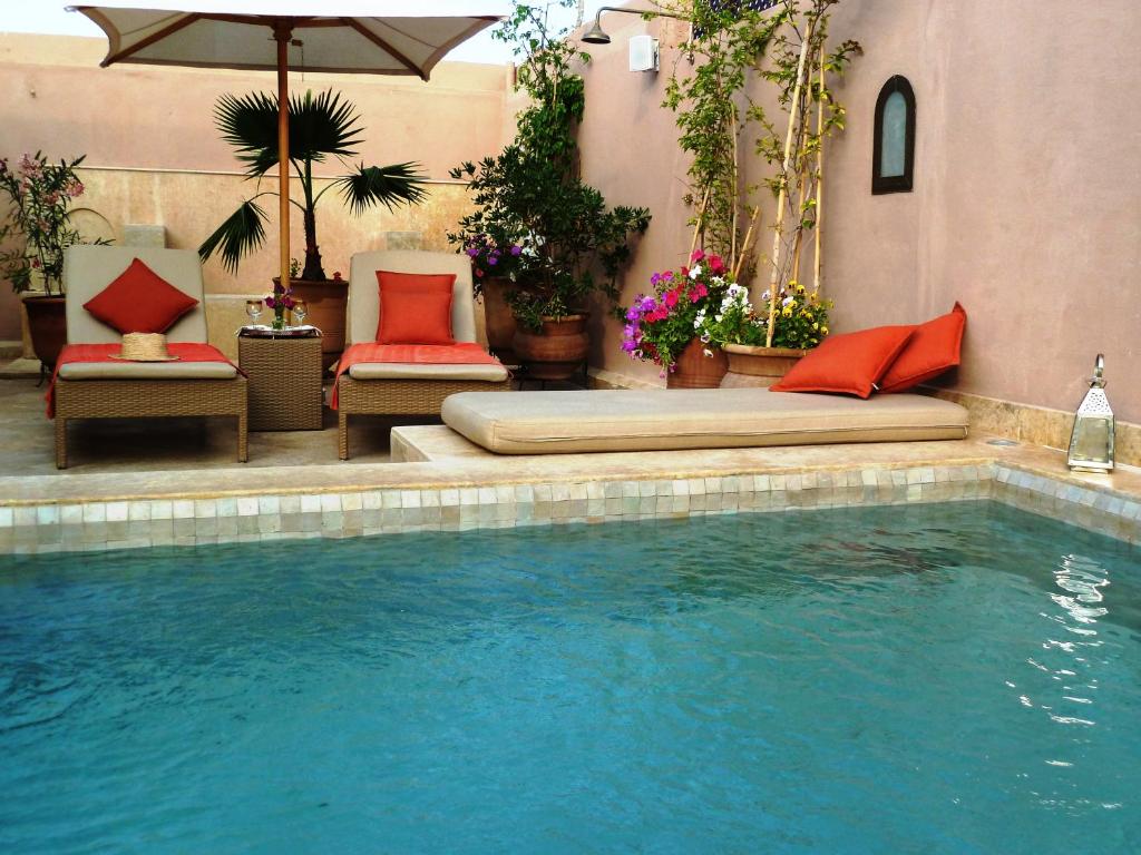 einen Pool mit zwei Stühlen und einem Bett neben einem Pool in der Unterkunft Riad Viva in Marrakesch