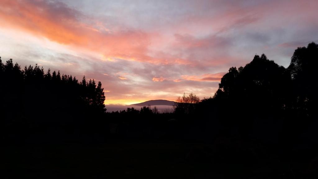 a sunset with trees and a mountain in the background at Posto Bello in North Loburn