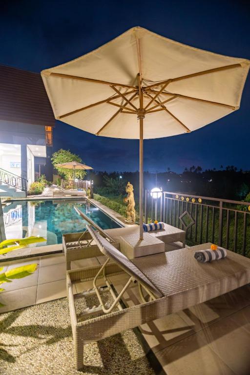 an umbrella and lounge chairs next to a swimming pool at The Pyramid Ubud River Villas in Gianyar