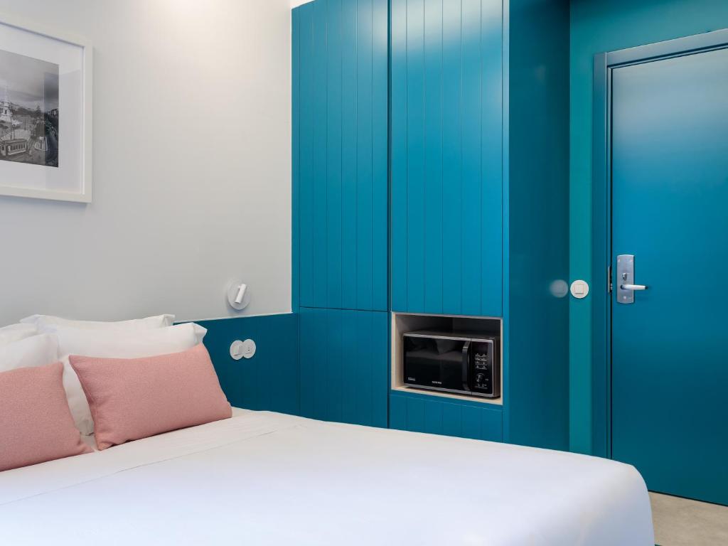A compact bedroom with a white bed, blue built-in cabinetry, and a blue entry door.