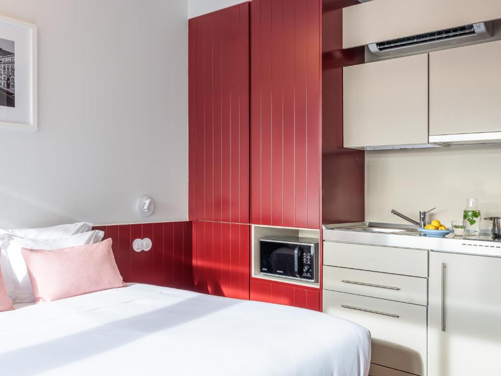 A bright bed-and-kitchenette studio with bold red cabinetry.