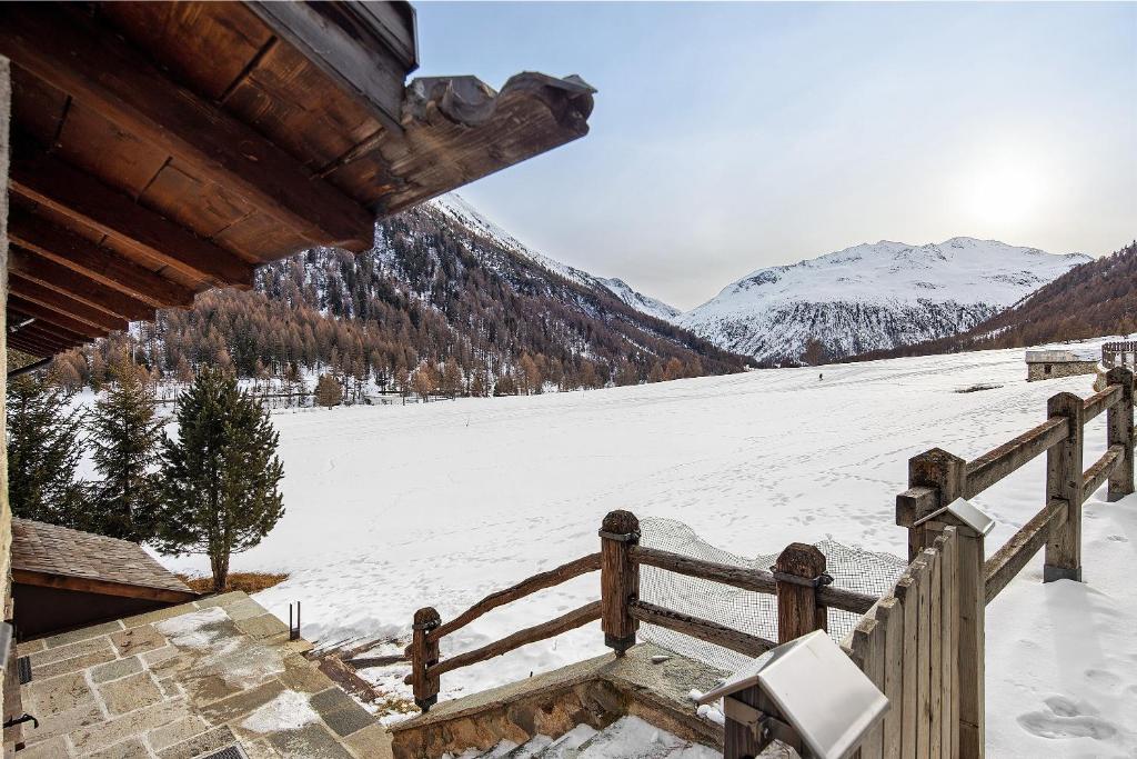 a snow covered field with a fence and snowy mountains at Tea da Anna e Luigi in Livigno