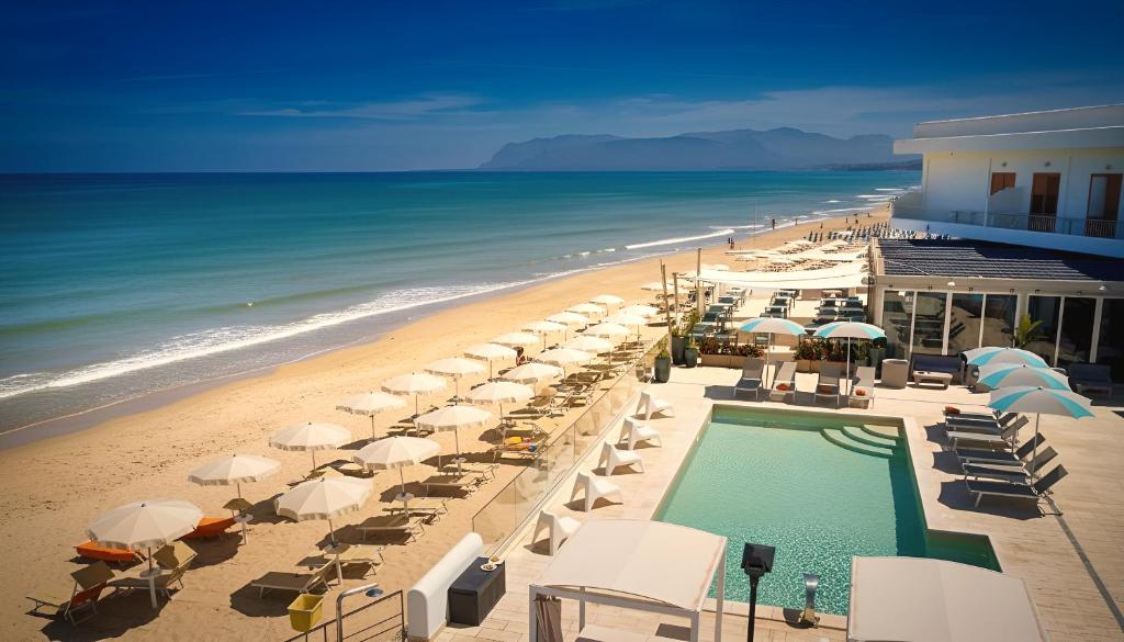 a beach with umbrellas and a swimming pool and the ocean at Hotel La Battigia in Alcamo Marina