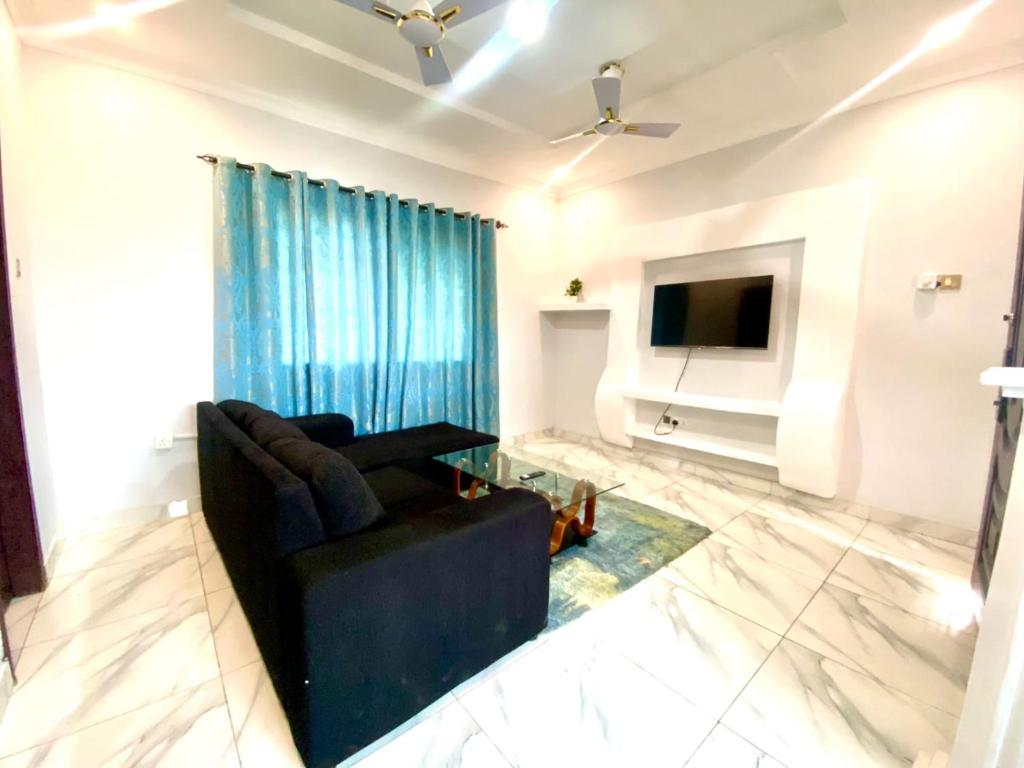 ein Wohnzimmer mit einer schwarzen Couch und einem Fernseher in der Unterkunft Happy Home in Weija