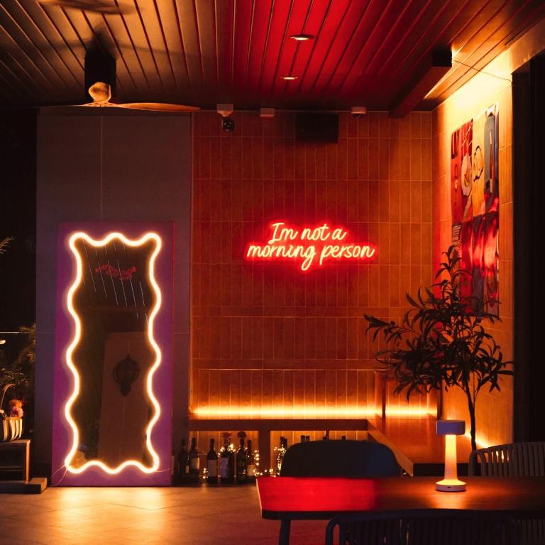 A dramatically lit lounge corner with a neon sign, bar shelving and statement artwork.