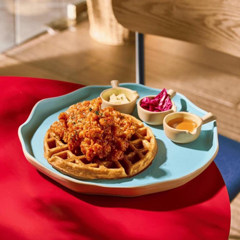 A waffle topped with fried chicken and served with sauces.