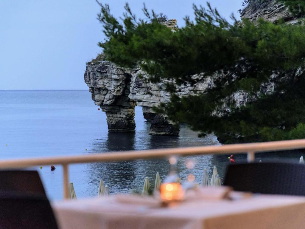 a table with a view of the ocean and a rock formation at Baia Delle Zagare - Handwritten Collection in Mattinata