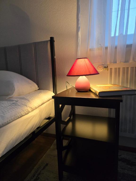 a red lamp on a table next to a bed at Ferienwohnung TALISA in Günzburg
