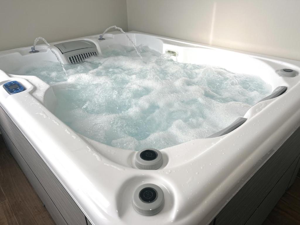 eine weiße Badewanne gefüllt mit blauem Wasser in der Unterkunft L'Hakuna II - Suite et Spa in Fontaine-Notre-Dame