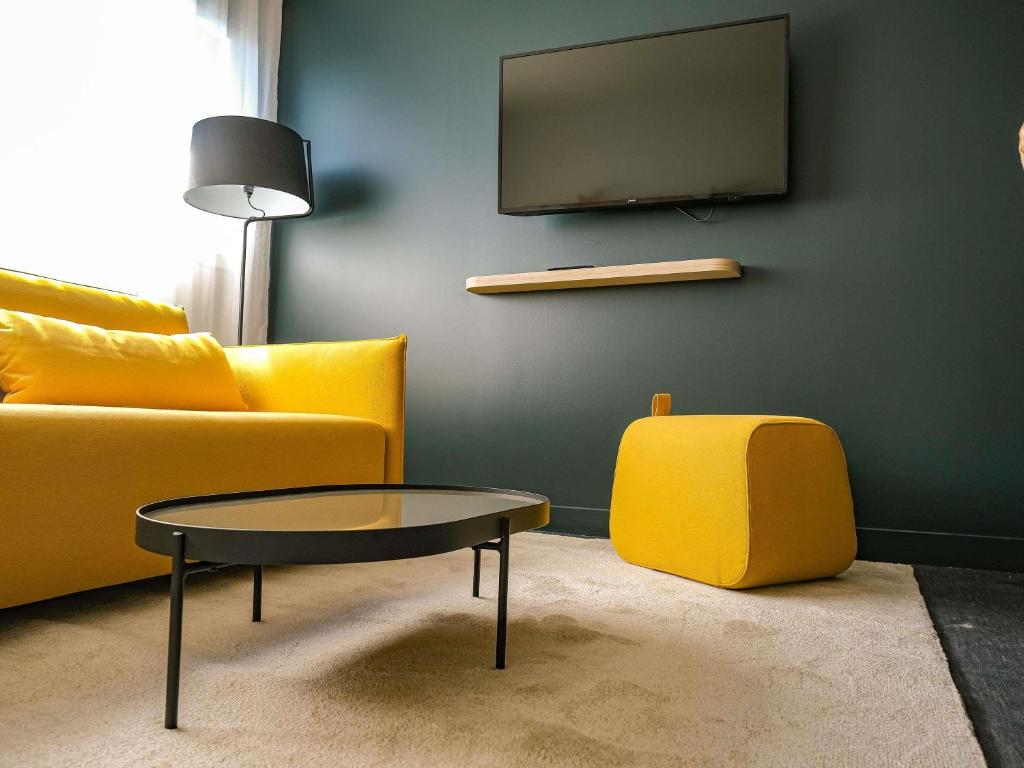 un salon avec un canapé jaune et une table dans l'établissement ibis Styles Bordeaux Lac Bruges, à Bordeaux