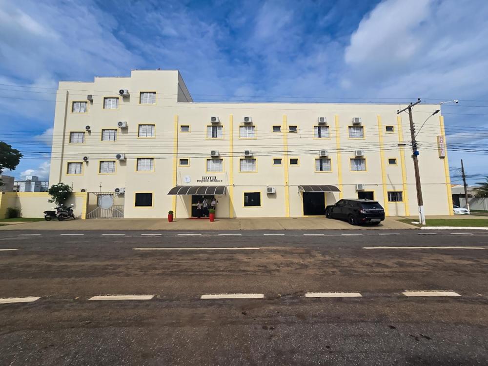 un grand bâtiment blanc avec une voiture garée devant. dans l'établissement Hotel Pequeno Mundo 2, à Campo Verde