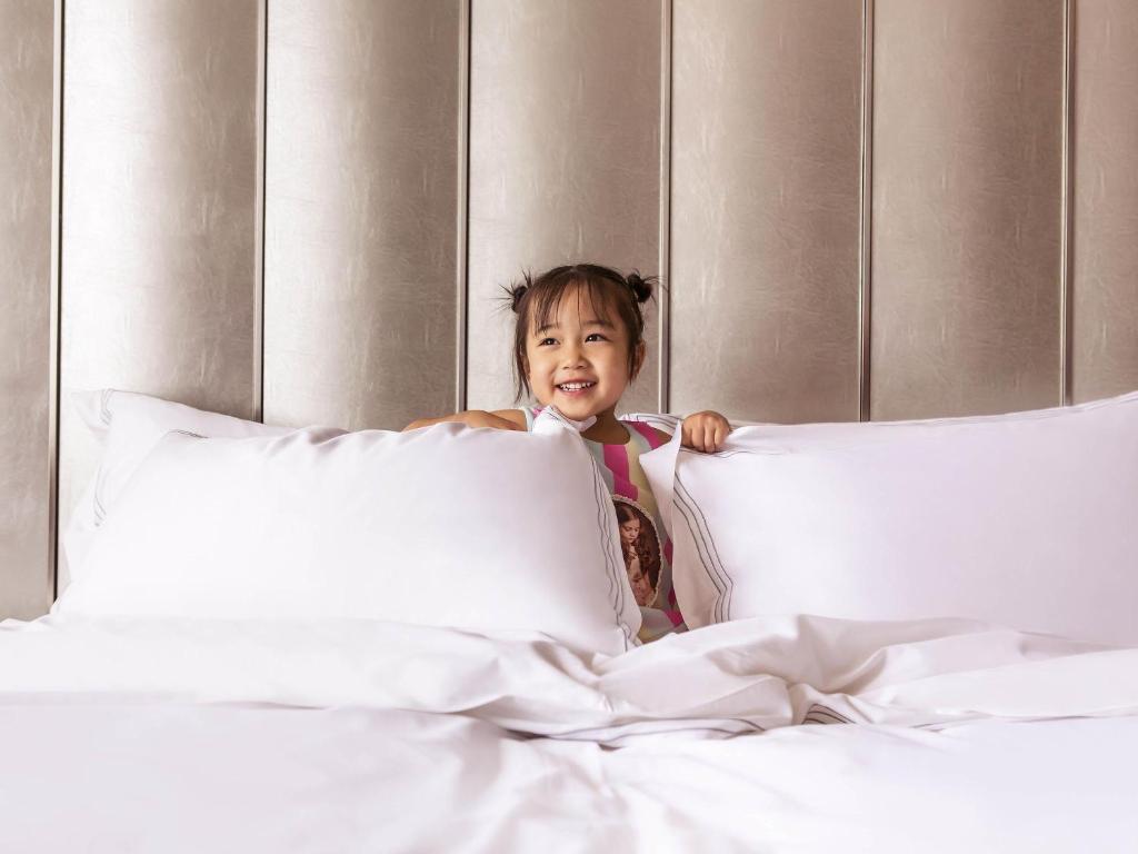 a little girl sitting on a bed at Novotel Daqing Haofang in Daqing