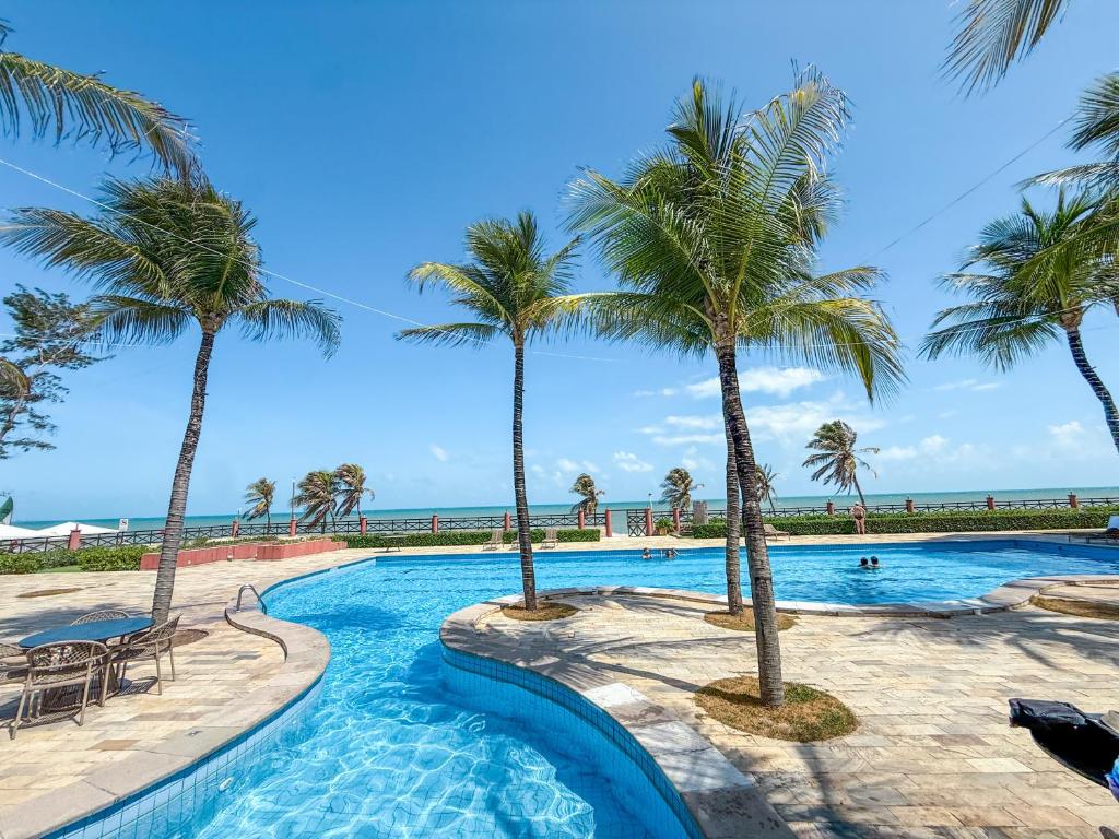 a pool with palm trees and the ocean at Kariri beach apt 427 Praia do Cumbuco in Cumbuco