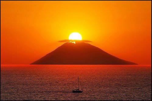 uma montanha no oceano com um barco ao pôr do sol em Casa&Mare em Pizzo