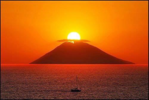 a mountain in the ocean with a boat at sunset at Casa&Mare in Pizzo