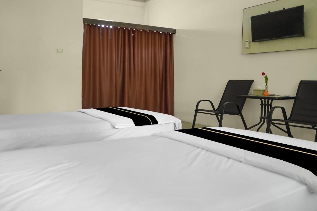 two beds in a hotel room with a table and chairs at Hotel O Roda Inn in Padang