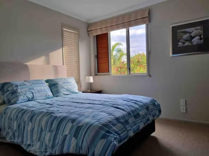 ein Schlafzimmer mit einem Bett mit blauer Bettdecke und einem Fenster in der Unterkunft Villa 46 in Pauanui