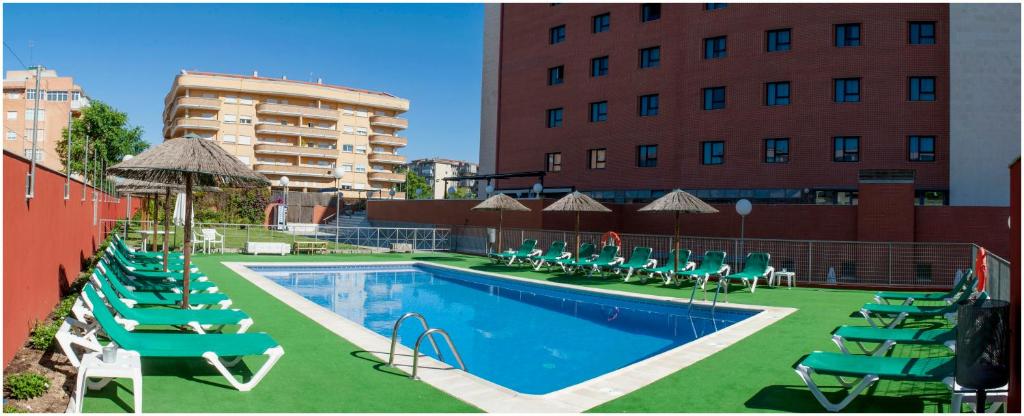 a pool with chairs and umbrellas next to a building at Extremadura Hotel in Cáceres