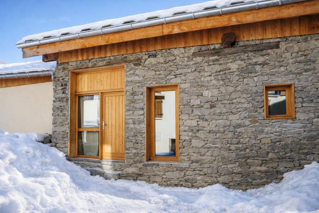 une maison en pierre avec des fenêtres dans la neige dans l'établissement Les Framboisiers by Lodji, à Saint-Marcel